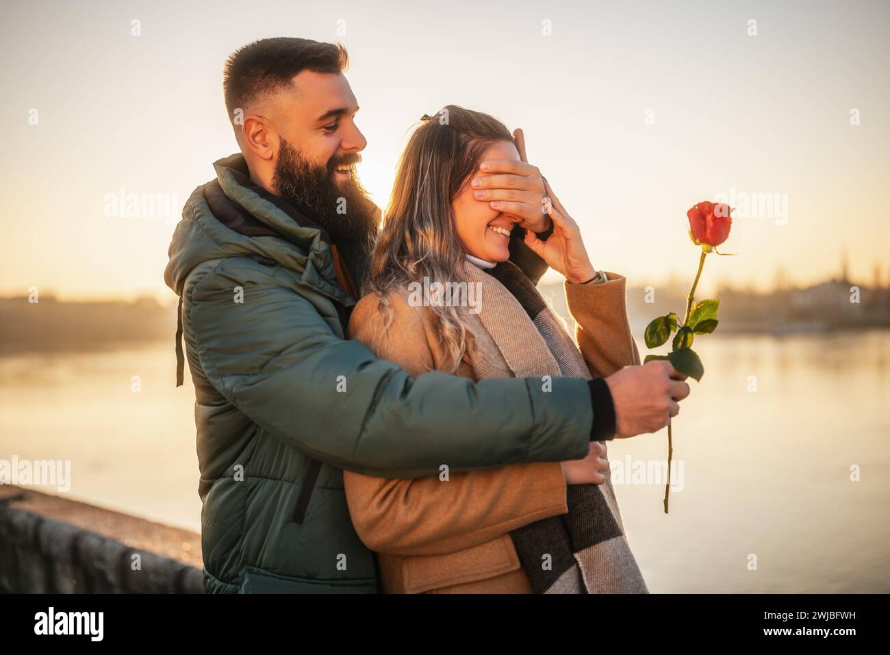 Homme heureux donnant rose rouge à sa femme pendant qu'ils aiment passer du temps ensemble sur un coucher de soleil. Banque D'Images