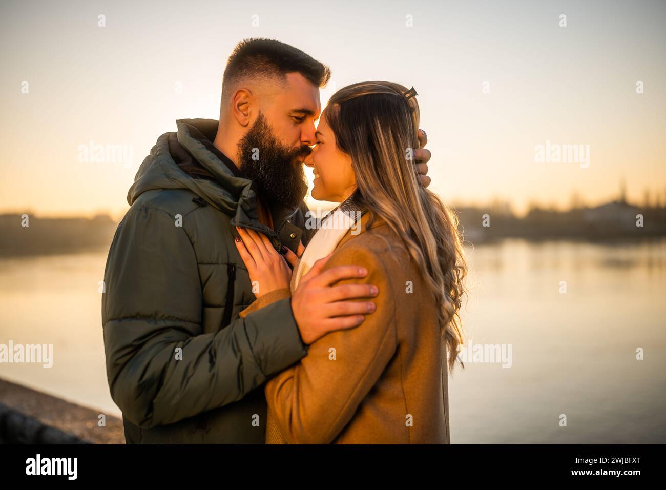Heureux couple profiter de passer du temps ensemble en plein air sur un coucher de soleil. L'homme embrasse sa femme dans le nez. Banque D'Images