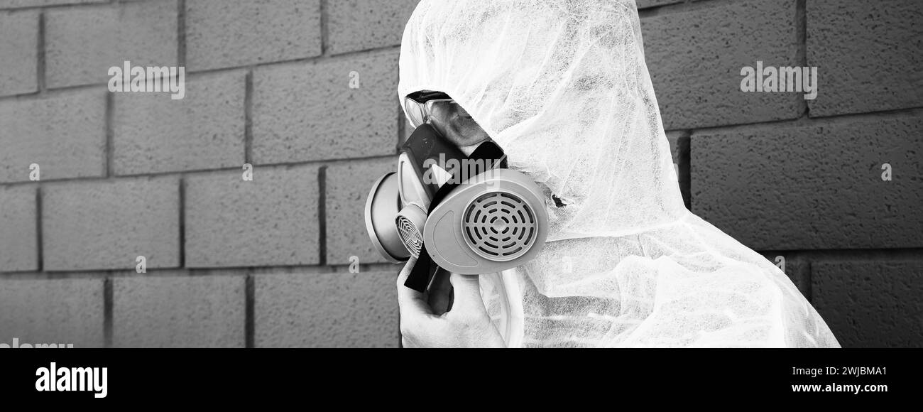 Bannière horizontale ou en-tête avec homme en vêtements de protection et un masque à gaz sur un fond gris urbain - travailleur pendant la désinfection et la décontaminatio Banque D'Images
