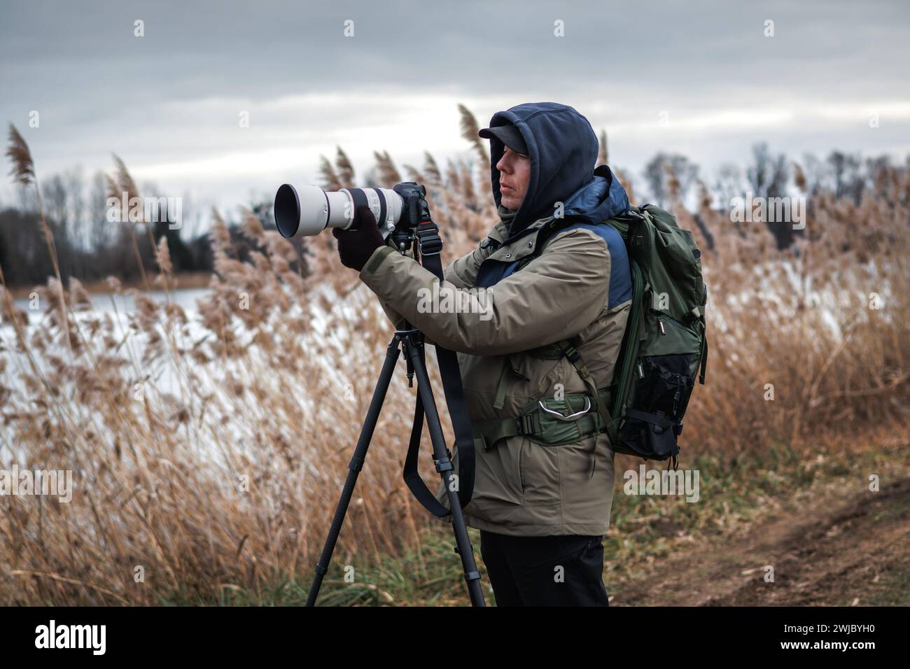 Le photographe installe l'appareil photo sur trépied à l'extérieur. Homme photographiant le paysage ou la faune au lac en hiver Banque D'Images