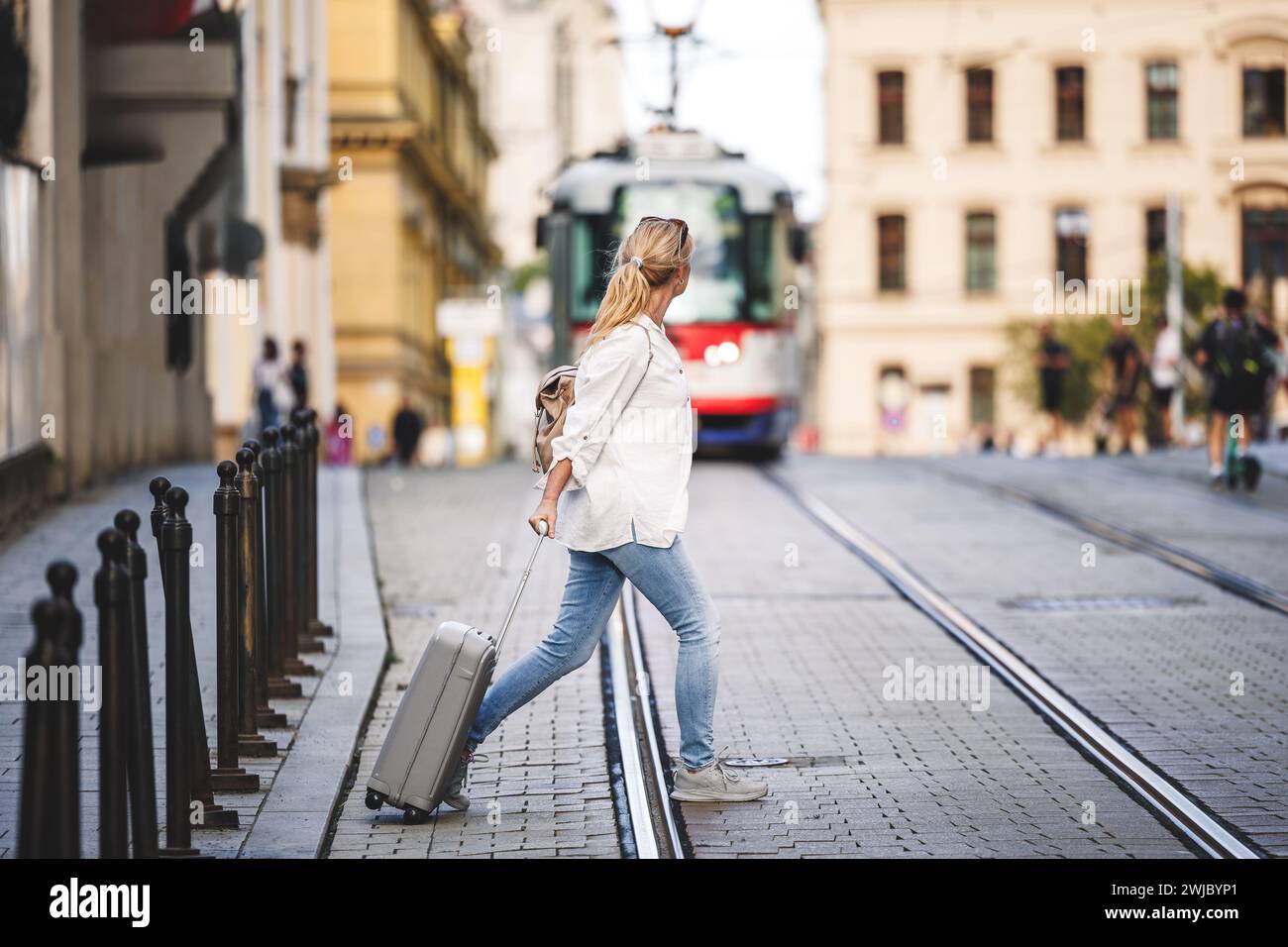 Femme touriste avec valise marche à travers la rue de la ville pendant que le tram arrive. Voyagez prudemment et en toute sécurité avec une assurance et évitez les accidents Banque D'Images