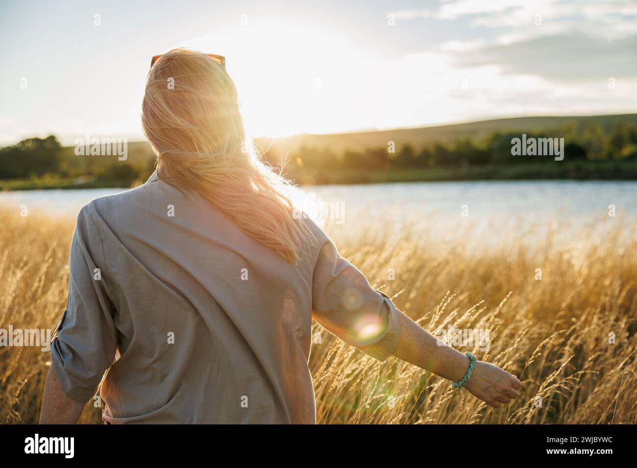 Femme détendue profitant de l'air frais au lac venteux pendant le coucher du soleil. Émerveillement, pleine conscience et joie de ce moment en plein air Banque D'Images