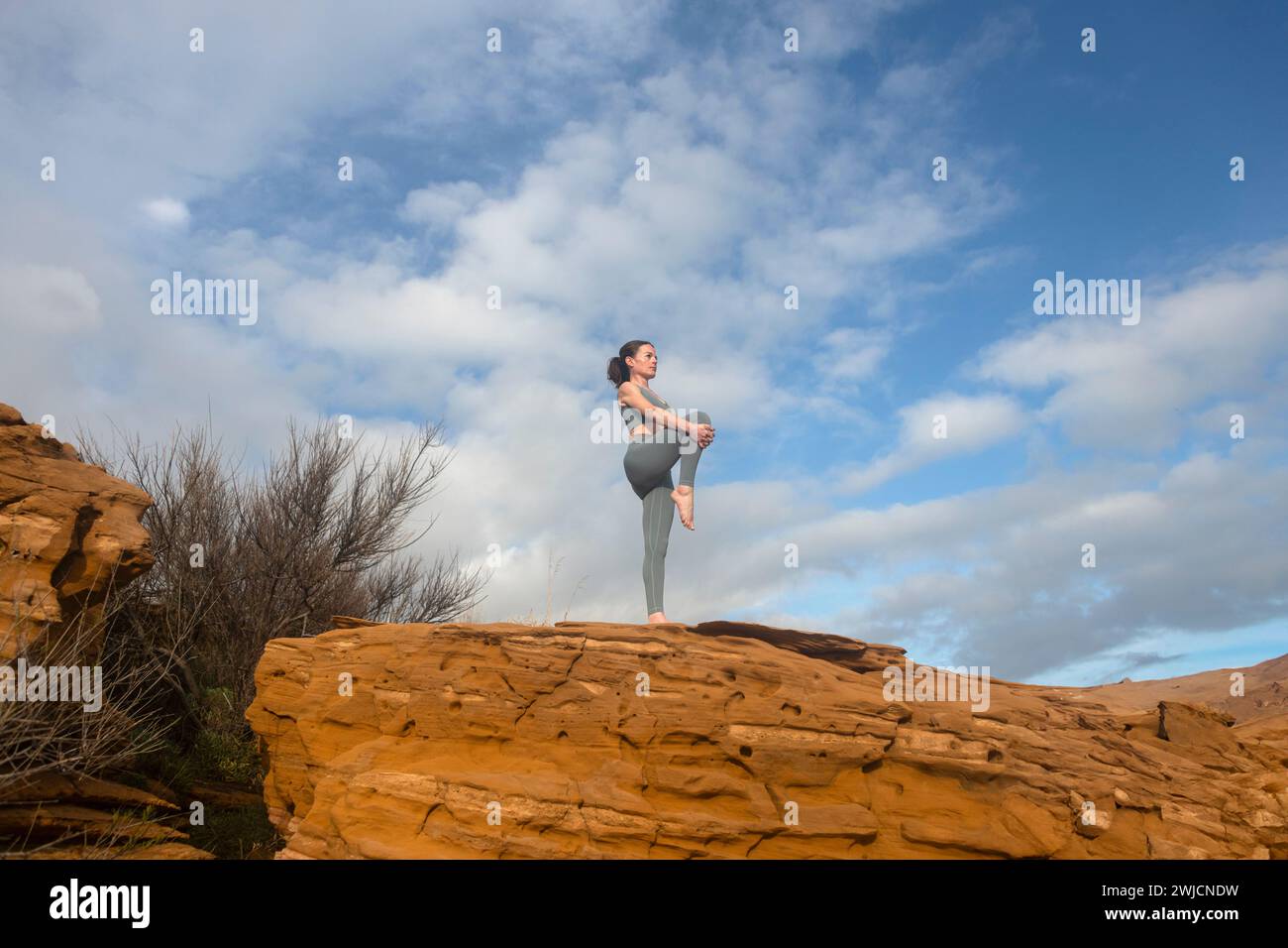 Femme sportive faisant des exercices d'échauffement d'étirement des jambes à l'extérieur sur le dessus des rochers rouges. Banque D'Images