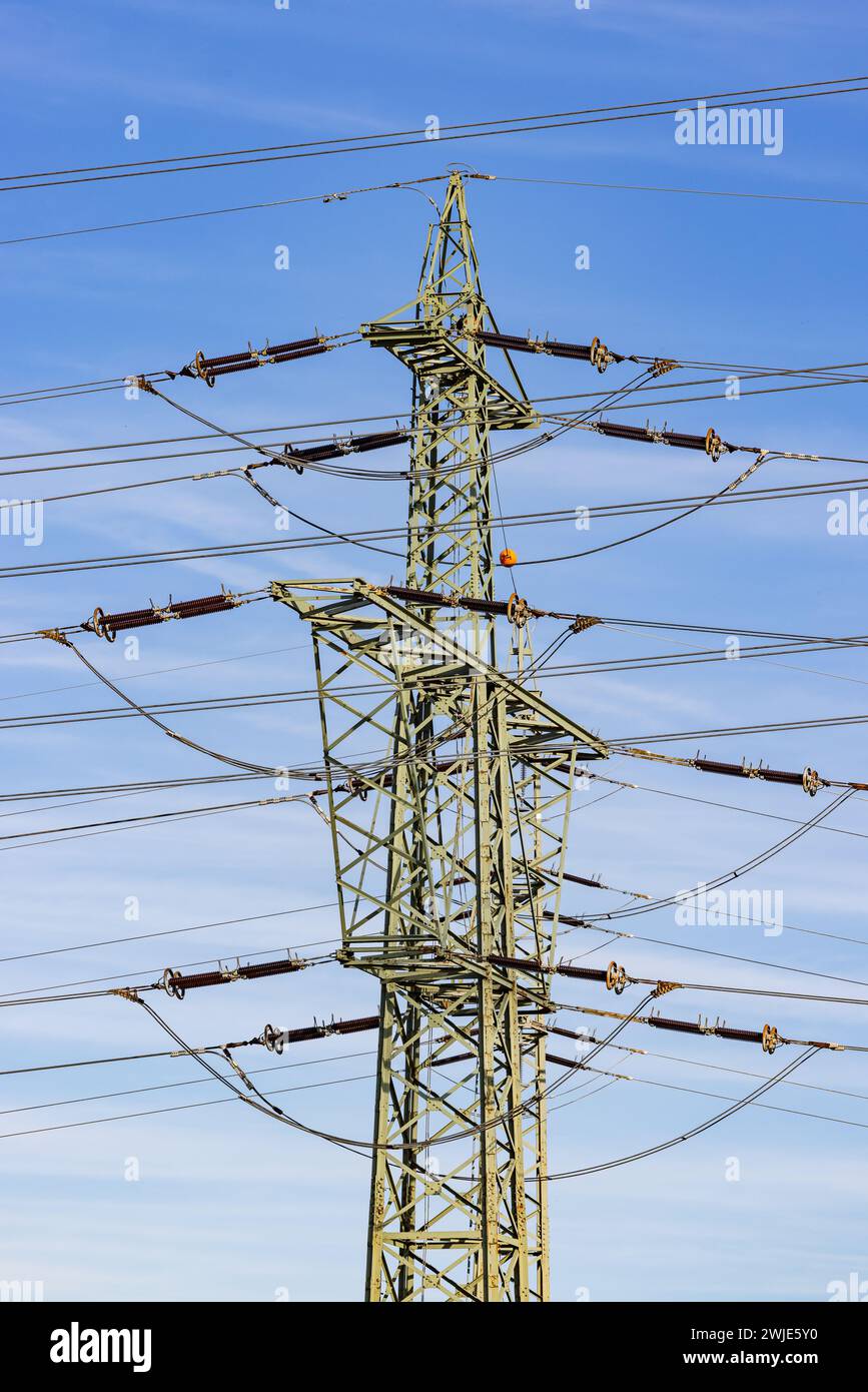 Un pylône haute tension avec isolants, traverses et câbles conducteurs ainsi que des lignes électriques aériennes devant un ciel bleu, photographie de portrait Banque D'Images