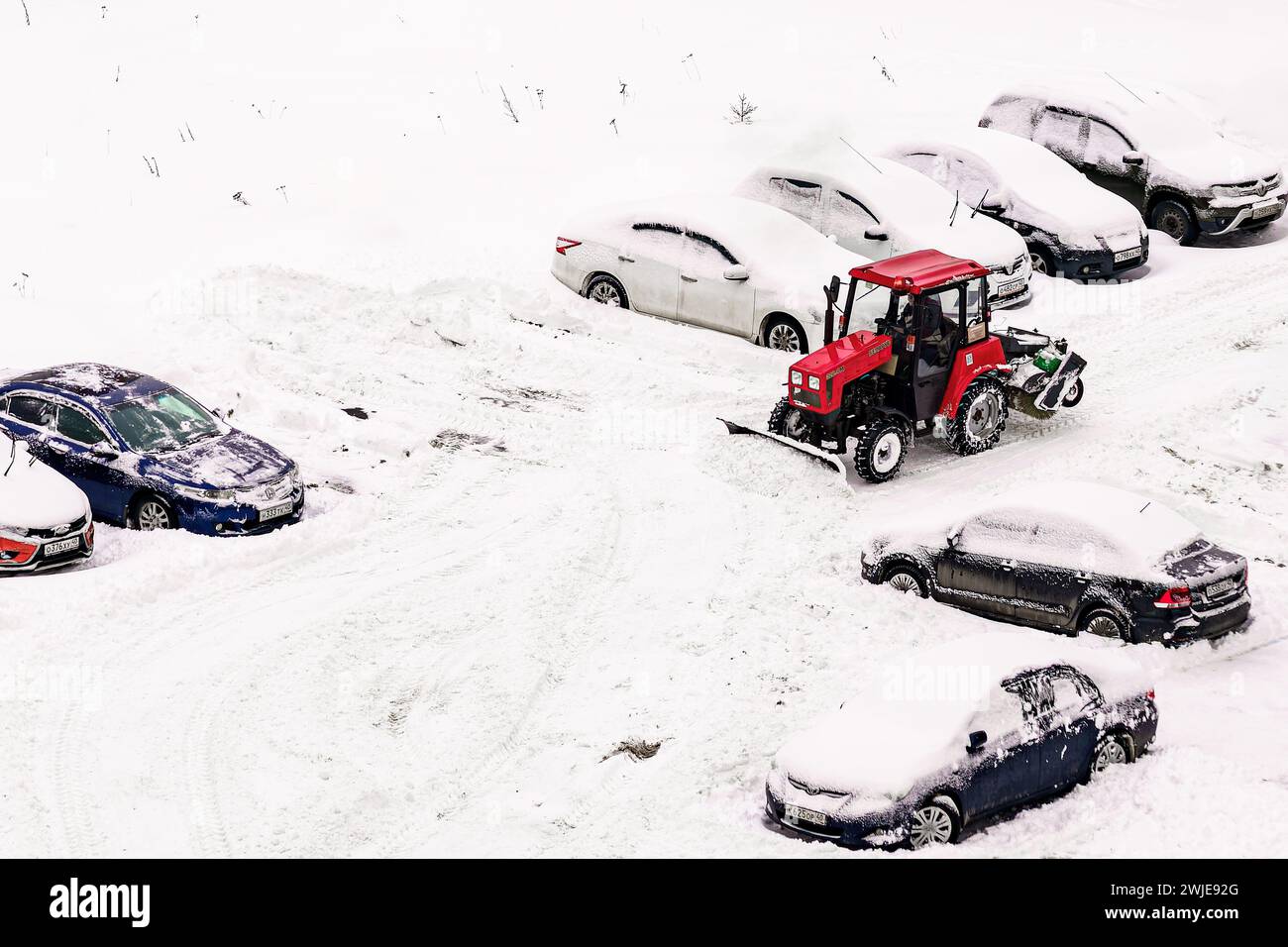 Kaluga, Russie - 8 décembre 2022 : tracteur rouge pelletant la neige avec un seau dans un parking après une chute de neige en hiver. Déneigement en ville. Banque D'Images