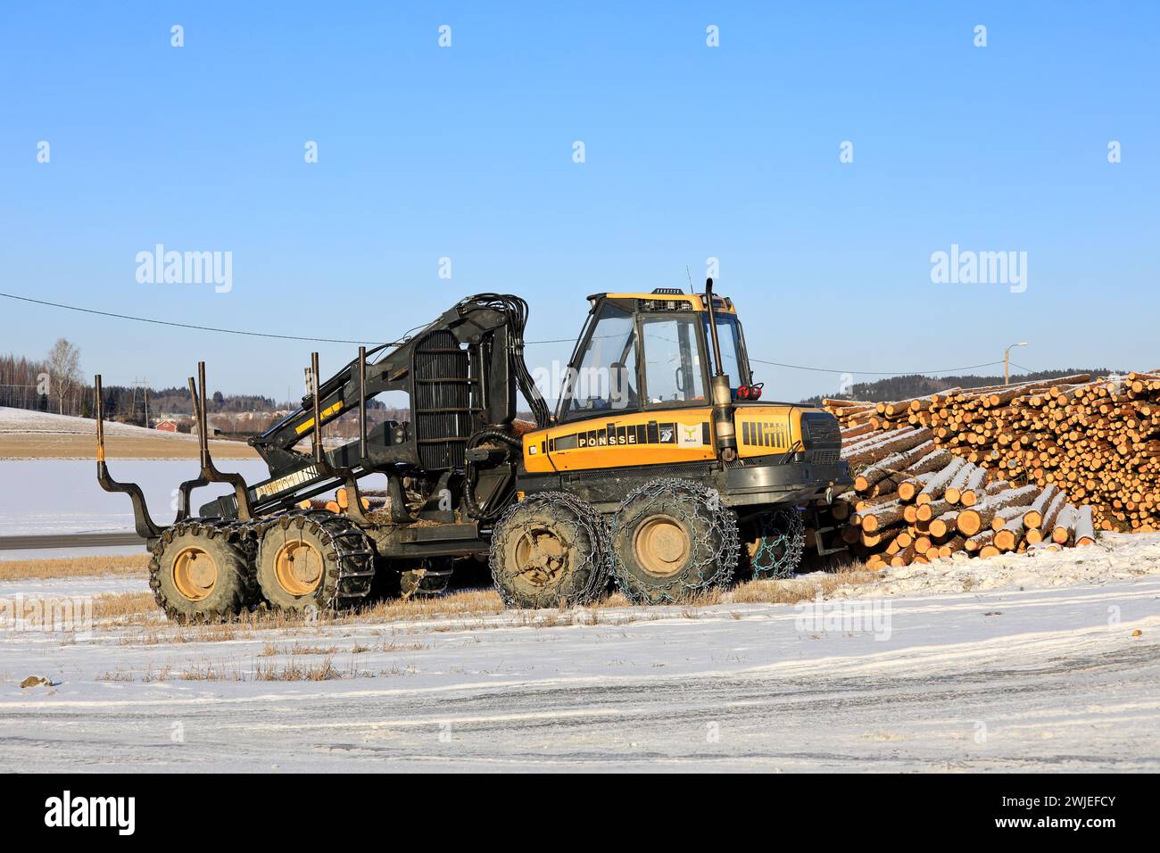 Transporteur forestier Ponsse Wise avec chaînes à neige sur pneus et grumes de pin empilées sur le chantier en hiver. Salo, Finlande. 9 février 2024. Banque D'Images