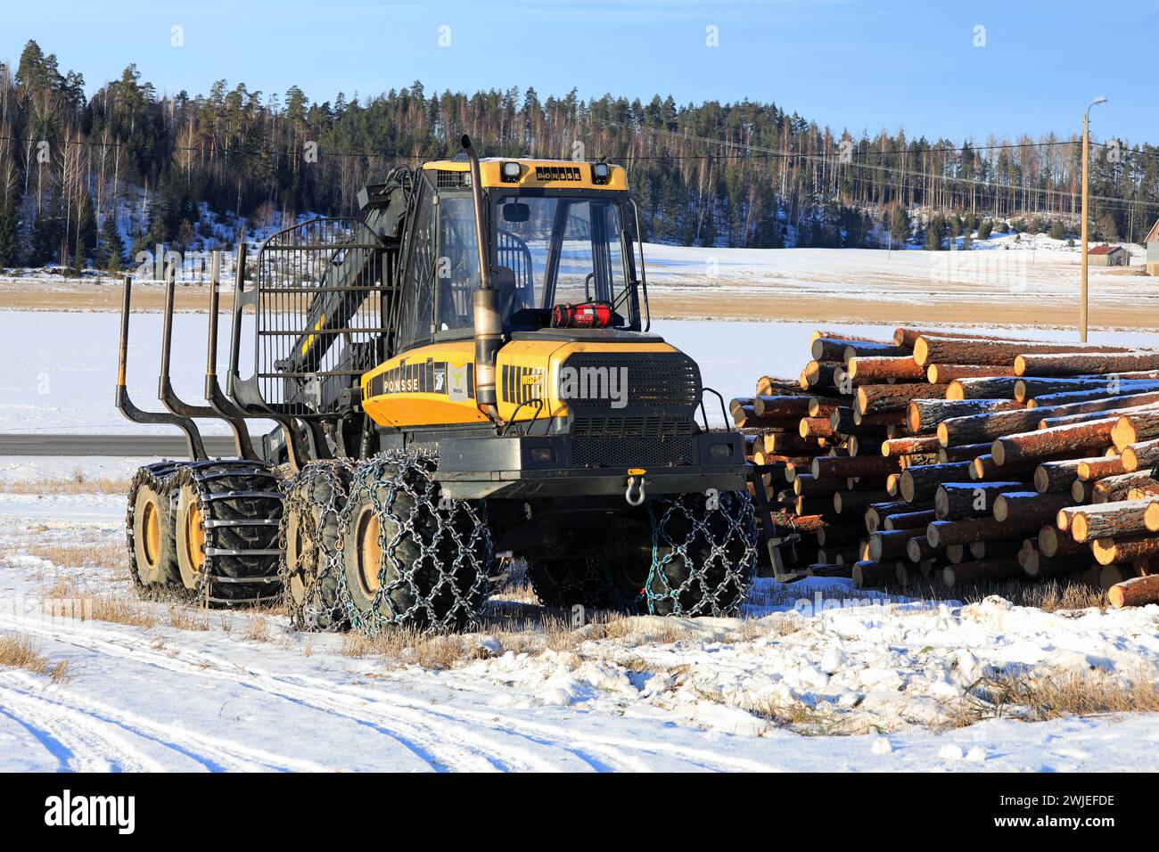 Porteur forestier Ponsse Wise avec chaînes à neige sur pneus et grumes de pin empilées sur un chantier glacé en hiver. Salo, Finlande. 9 février 2024. Banque D'Images