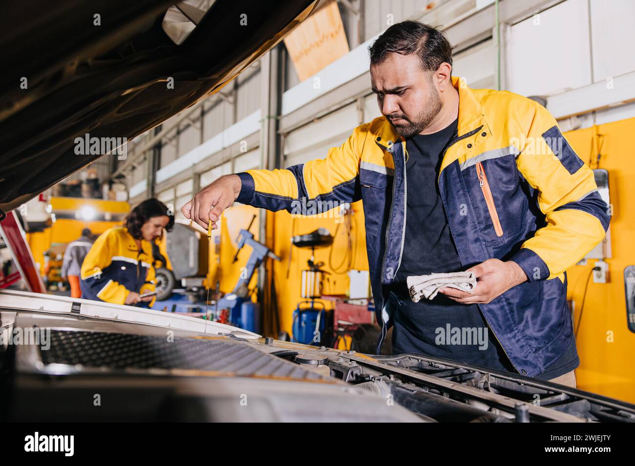 Le travailleur de mécanicien automatique de garage travaille vérifier le bâton de niveau d'huile moteur dans le travail d'équipe d'employé de centre de service de voiture Banque D'Images