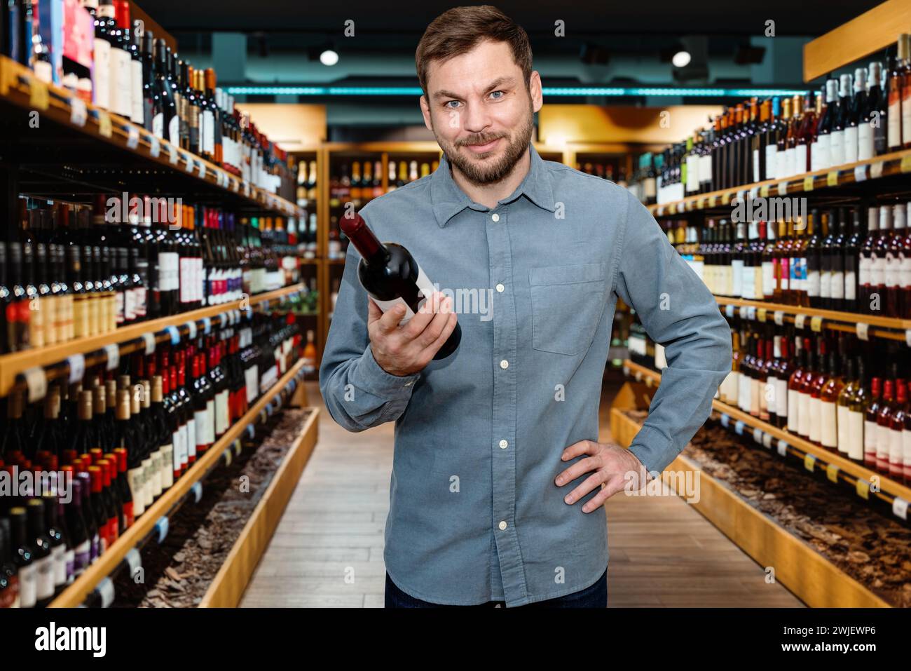 L'homme choisit un vin dans un magasin d'alcool et souriant. Bannière de vente au détail pour les vignerons et les détaillants de vin. Banque D'Images