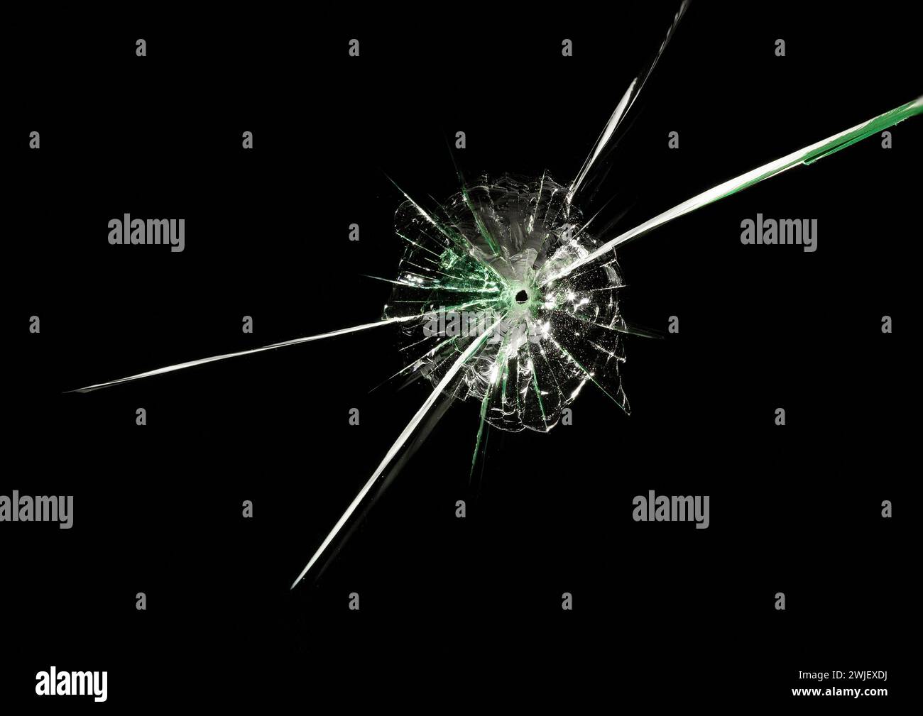 Trou de balle dans le verre avec de longues fissures croisées et des reflets verts sur fond noir. Macro. Gros plan. Banque D'Images