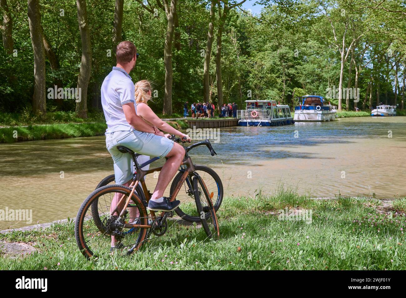 Couple sur une balade à vélo le long du canal, péniche et maison de gardien d'écluse convertie en restaurant "la bonne Planque". Le canal du midi est enregistré Banque D'Images