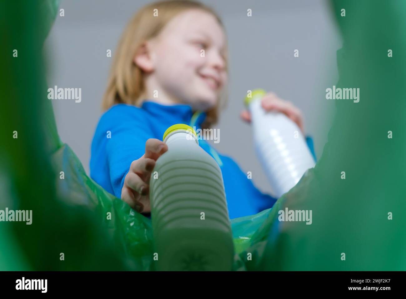 Vue à angle bas un enfant triant la corbeille en plastique à la maison. Élimination des produits de bouteilles de lait Banque D'Images Vue à angle bas un enfant triant la corbeille en plastique à la maison. Élimination des produits de bouteilles de lait Banque D'Images