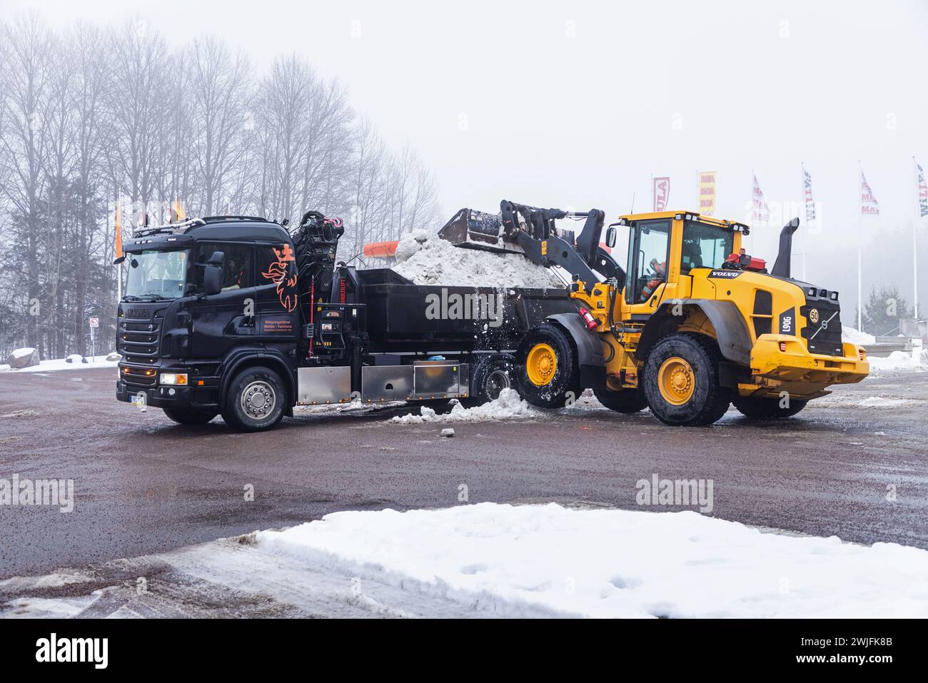 Météo saisonnière, une chargeuse sur pneus chargeant la neige pour la déneiger avec un camion jeudi à Motala, en Suède. Banque D'Images