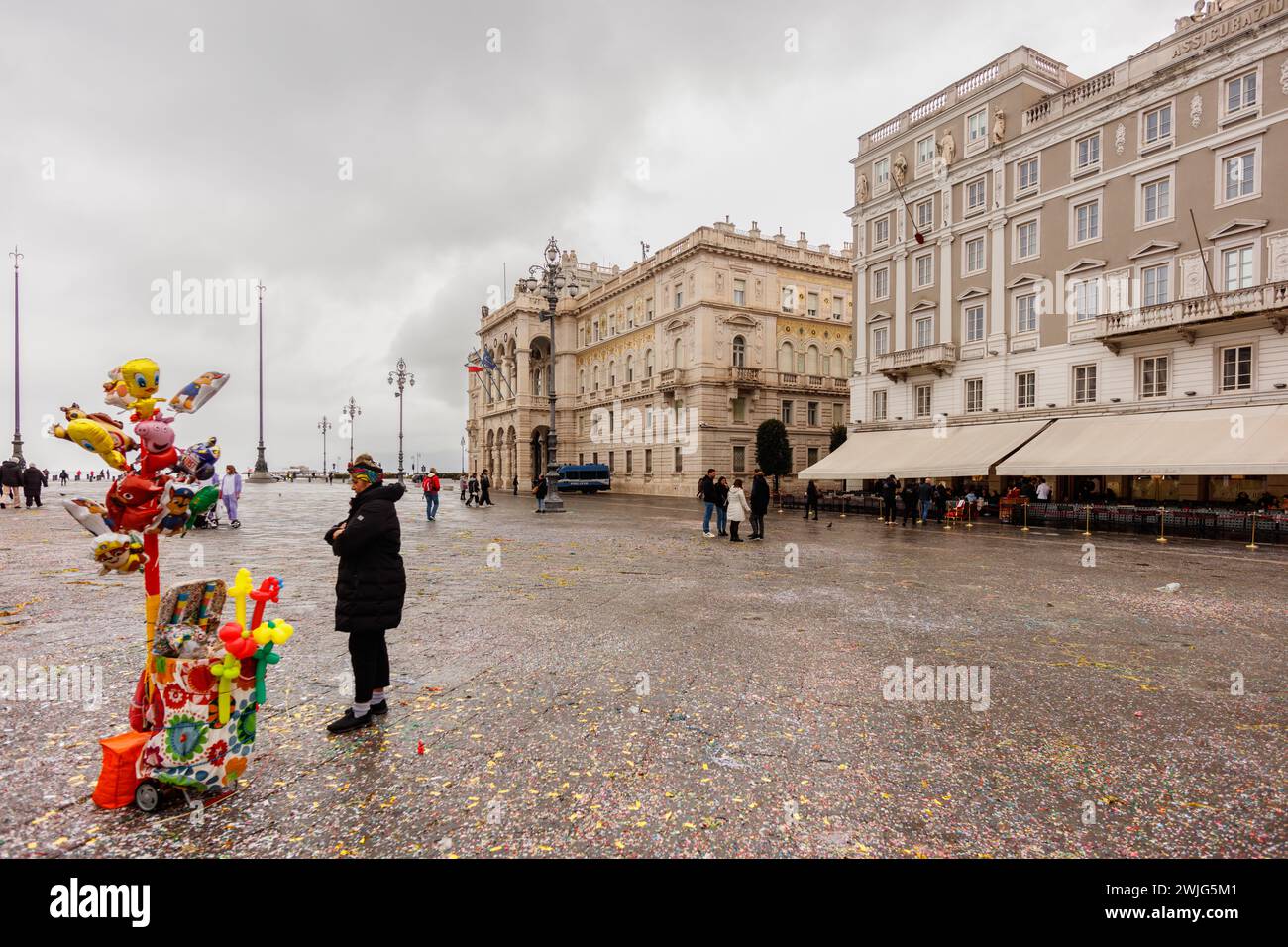 Trieste, Italie - 11 février 2024 : la place principale (Piazza Unità d'Italia) dans un jour de pluie, avec un vendeur de ballons. Banque D'Images