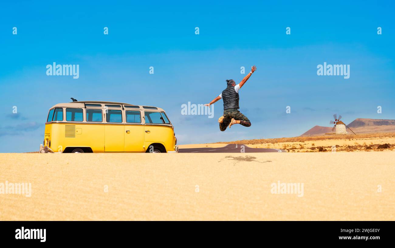 Homme voyageur heureux sautant dans les dunes de sable d'un paysage désertique - homme surfer solo voyageant dans un camping-car classique aux îles Canaries, Espagne Banque D'Images