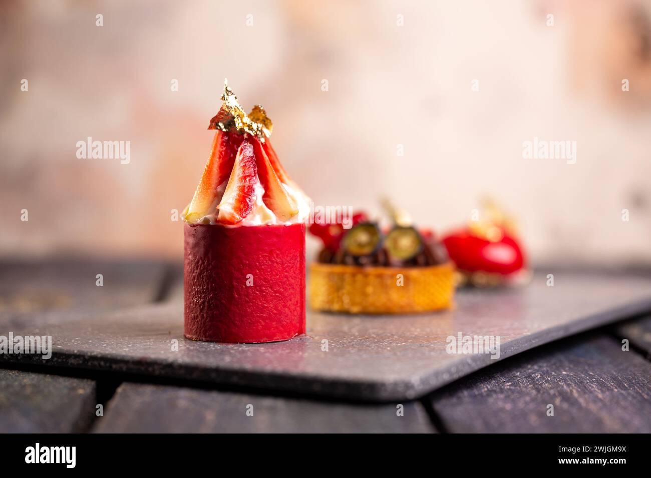 Tarte au chocolat gourmande, mousse à la fraise, macaron à la framboise sur planche en ardoise avec fond rose pour un élégant affichage de dessert. Banque D'Images