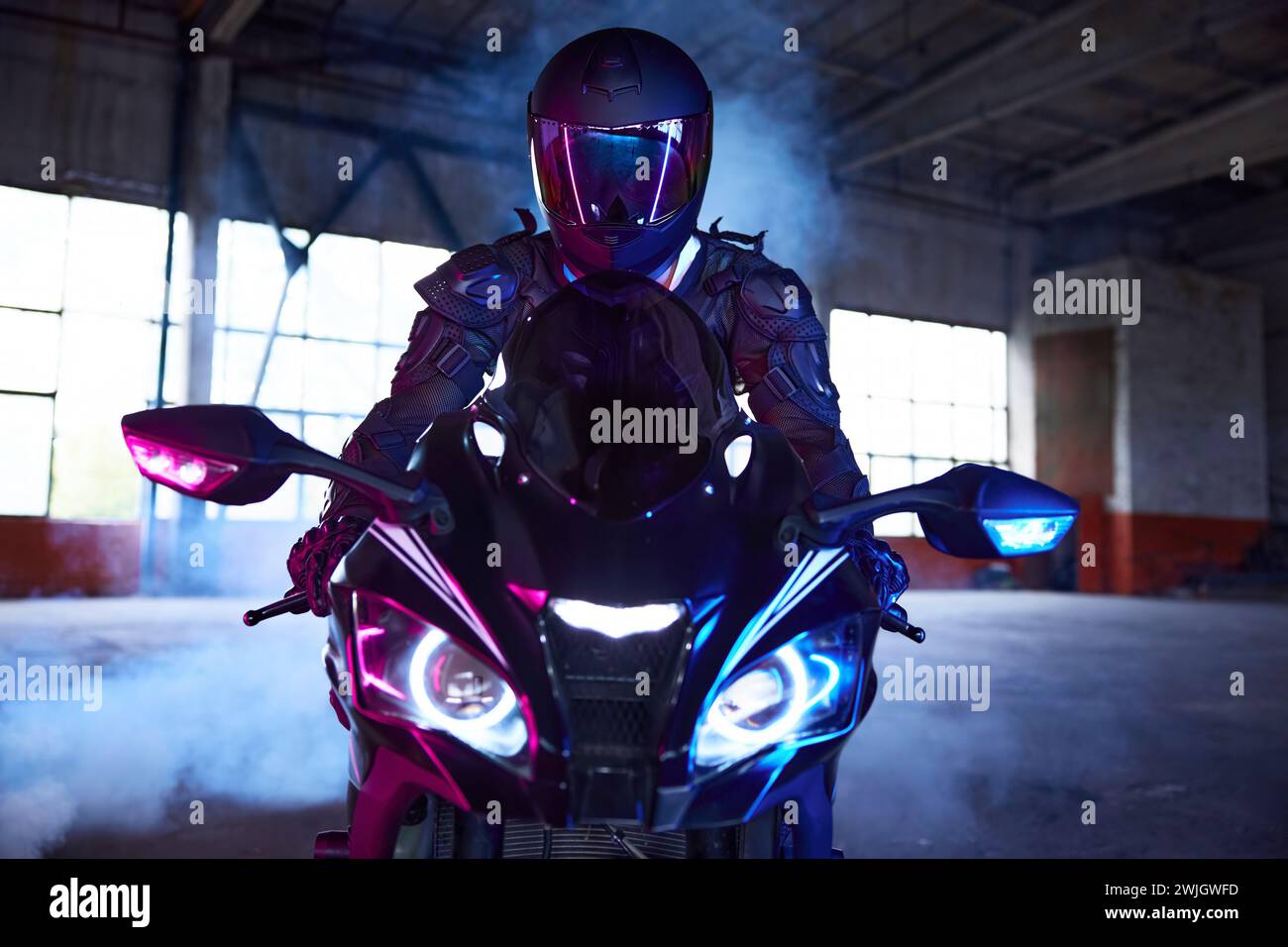 Portrait de vue de face de motard conduisant moto sportive dans la lumière néon Banque D'Images
