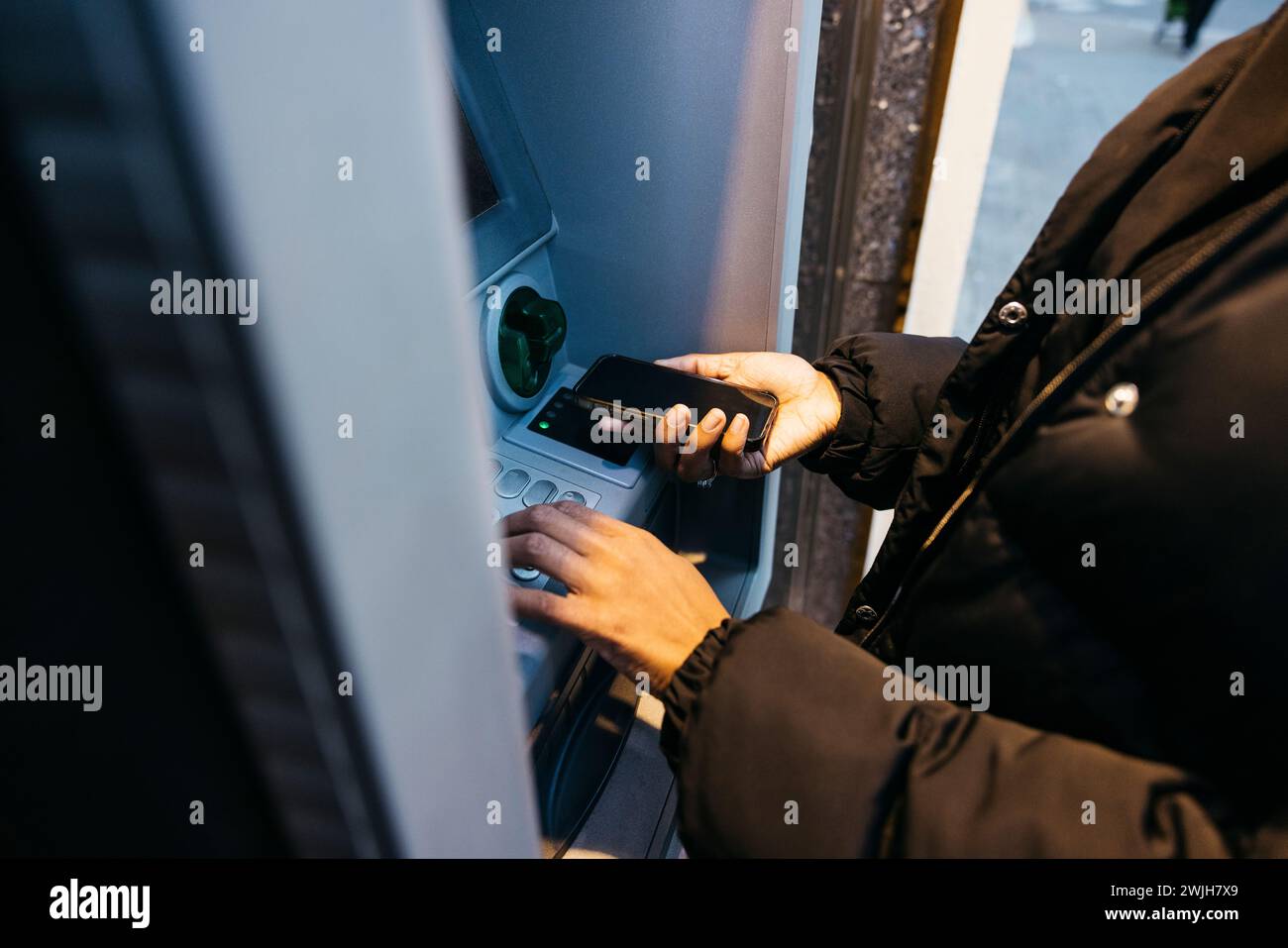 Gros plan des mains d'une femme à l'aide d'un smartphone avec technologie sans contact à un guichet automatique. Prendre de l'argent d'un caissier avec un téléphone. Banque D'Images