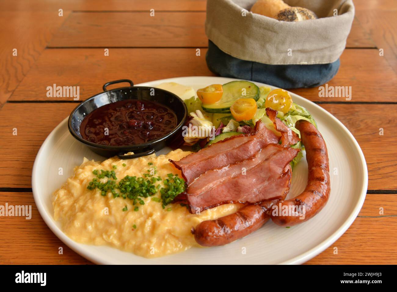 Petit déjeuner polonais avec bacon, saucisses, œufs brouillés, salade fraîche, confiture, beurre, et panier de pain sur la table en bois, Pologne, UE Banque D'Images