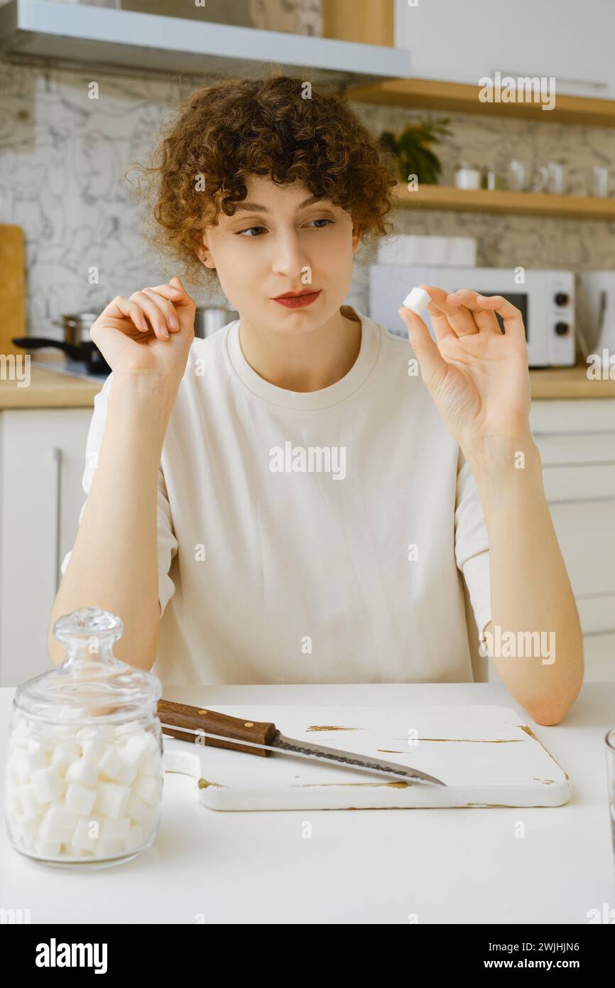 Femme courageuse regarde un morceau de sucre voulant réduire la quantité de bonbons dans sa nourriture Banque D'Images