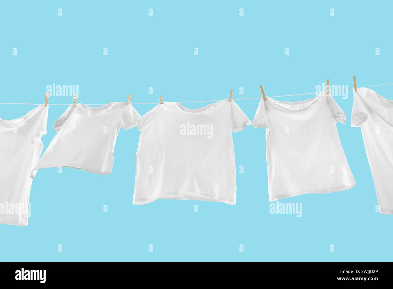 T-shirts séchant sur la ligne de lavage sur fond bleu clair, vue d'angle bas Banque D'Images T-shirts séchant sur la ligne de lavage sur fond bleu clair, vue d'angle bas Banque D'Images