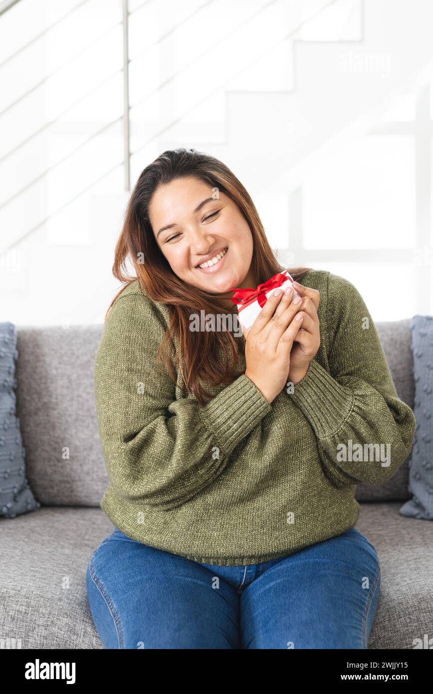 Jeune femme biraciale sourit tenant un petit cadeau à la maison sur un appel vidéo Banque D'Images