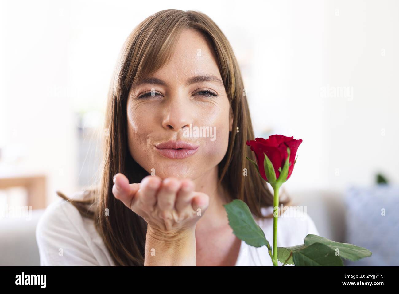 Une femme caucasienne d'âge moyen souffle de façon ludique un baiser tout en tenant une rose rouge Banque D'Images