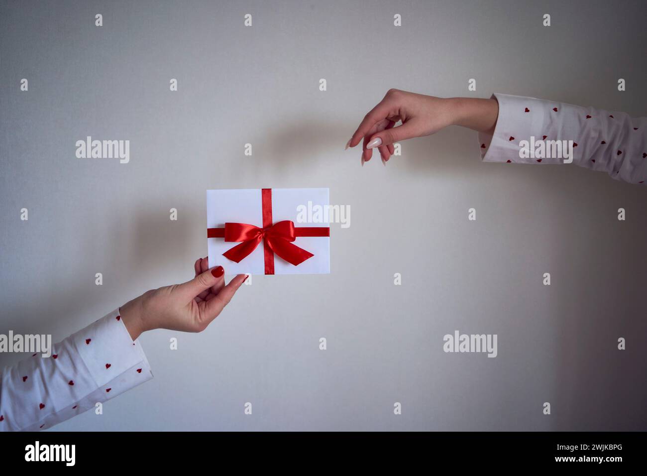 certificat cadeau en couleurs rouge et blanc dans les mains féminines sur un mur blanc Banque D'Images