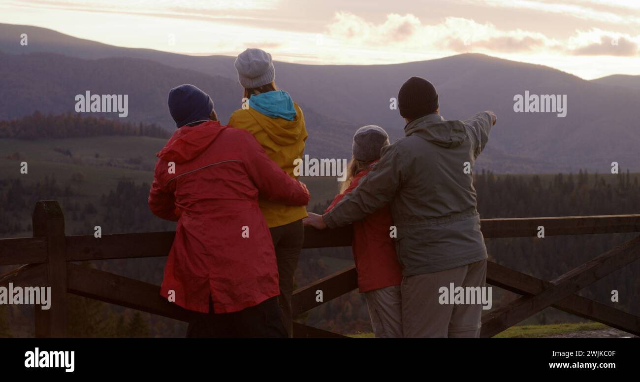 Les copains de randonnée se tiennent près d'une clôture en bois et regardent le coucher du soleil. Groupe de divers touristes ou voyageurs apprécient le paysage des montagnes et la belle nature pendant le voyage. Passionnés d'activités de plein air. Ralenti. Banque D'Images