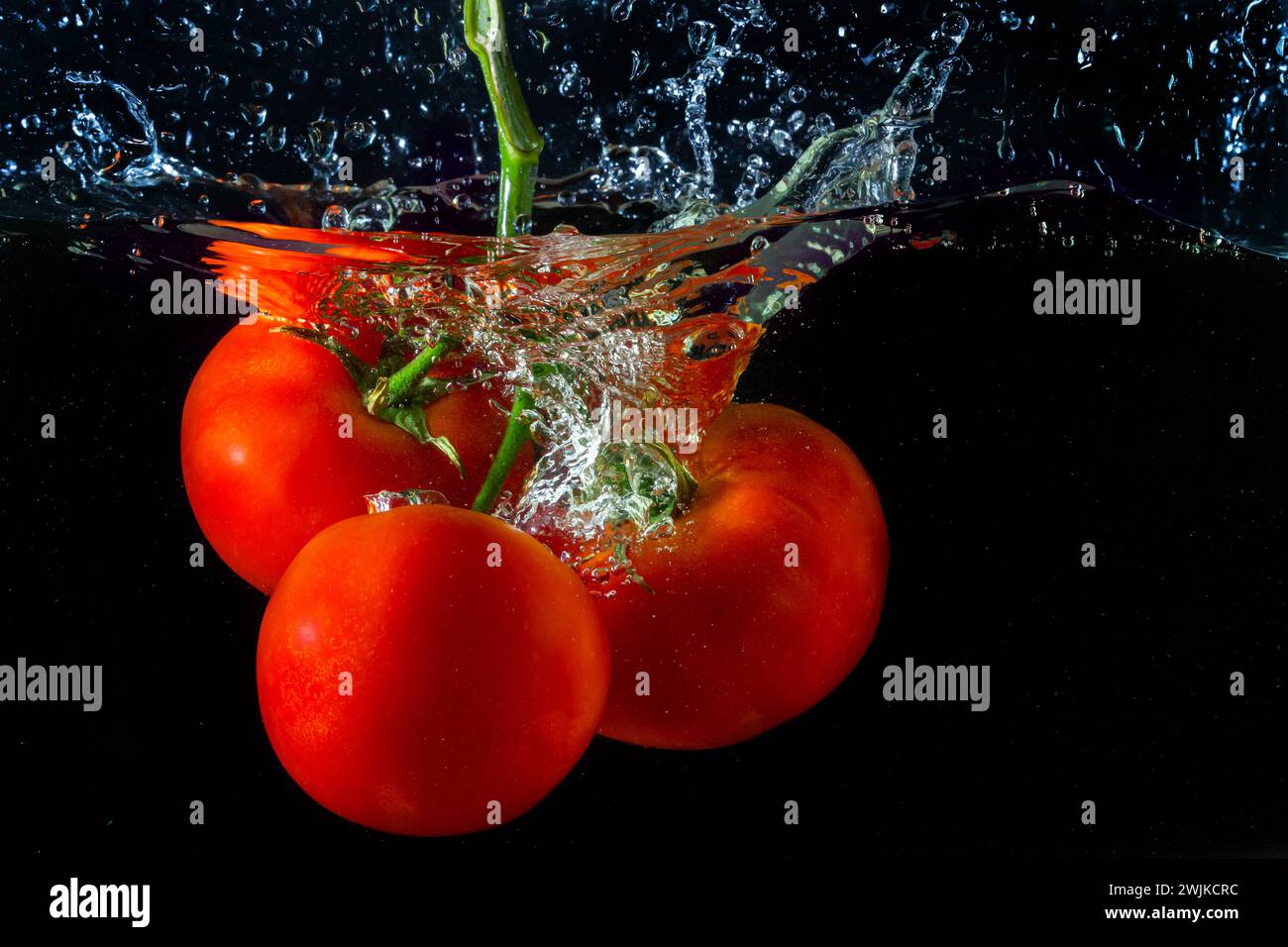 Tomate rouge fraîche tombant dans l'eau avec des éclaboussures d'eau et des bulles d'air isolées sur fond noir. Banque D'Images