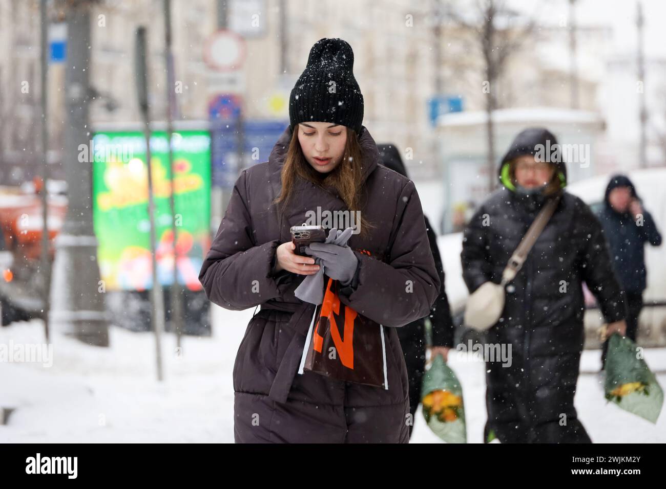 Jeune femme marchant avec smartphone dans les mains sur la rue de la ville d'hiver pendant la neige Banque D'Images
