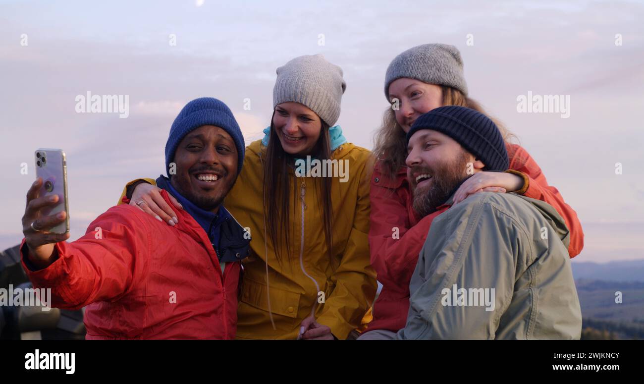 Les copains de randonnée se tiennent près d'une clôture en bois et regardent le coucher du soleil. Groupe de divers touristes ou voyageurs apprécient le paysage des montagnes et la belle nature pendant le voyage. Passionnés d'activités de plein air. Ralenti. Banque D'Images