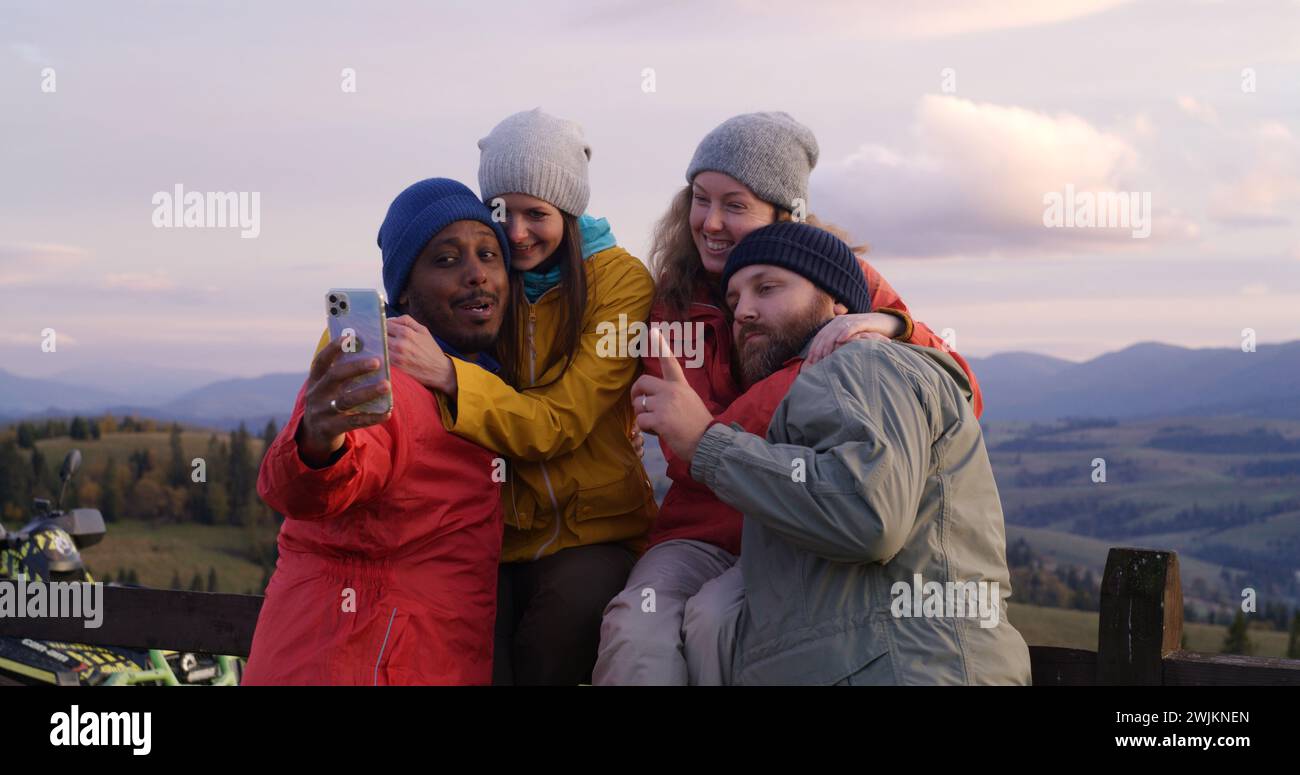 Les copains de randonnée se tiennent près d'une clôture en bois et regardent le coucher du soleil. Groupe de divers touristes ou voyageurs apprécient le paysage des montagnes et la belle nature pendant le voyage. Passionnés d'activités de plein air. Ralenti. Banque D'Images