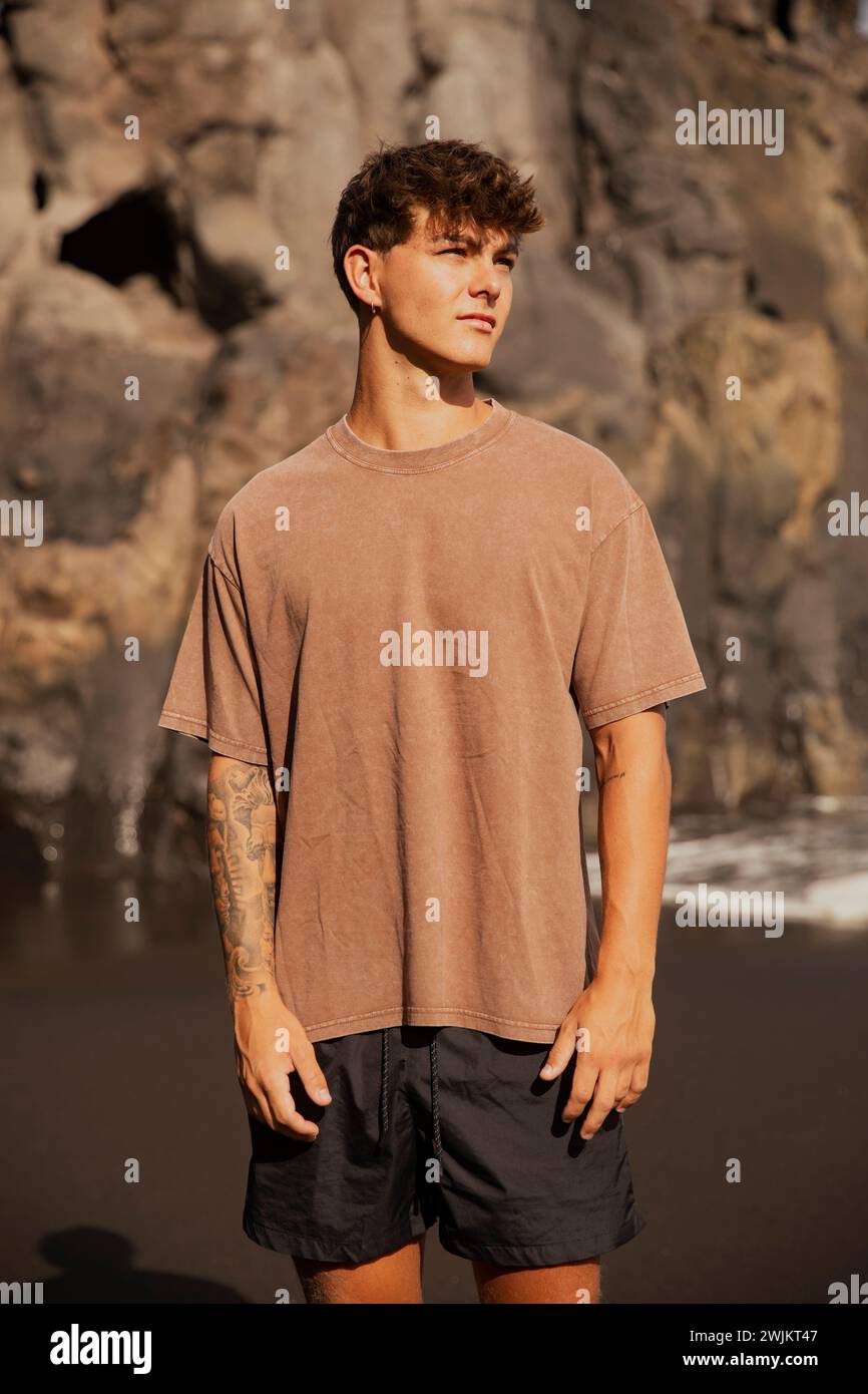 Portrait de beau gars tatoué avec des cheveux bruns posant sur la plage Banque D'Images