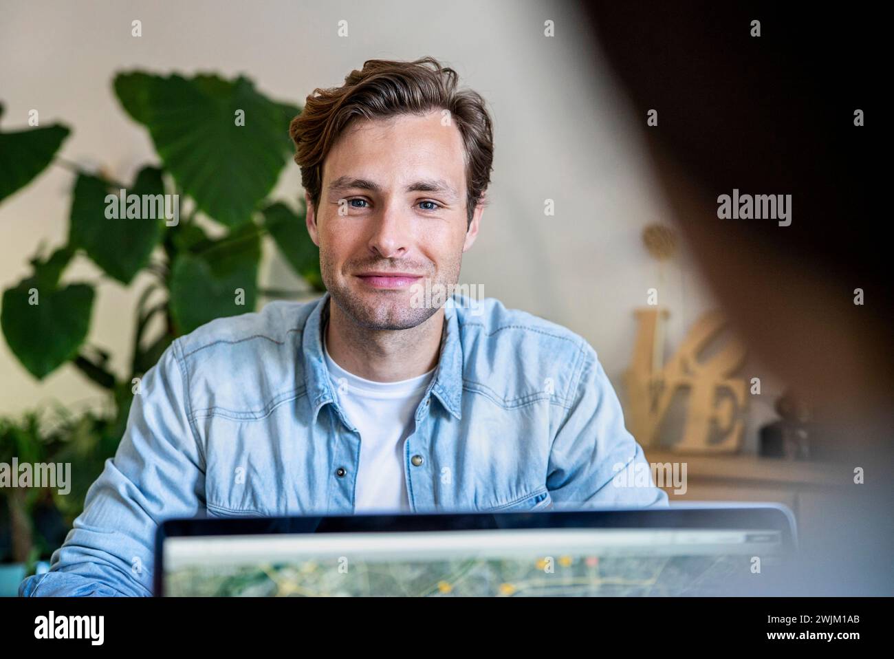Graphiste masculin regardant la caméra tout en étant assis au bureau à l'aide d'un ordinateur portable Banque D'Images