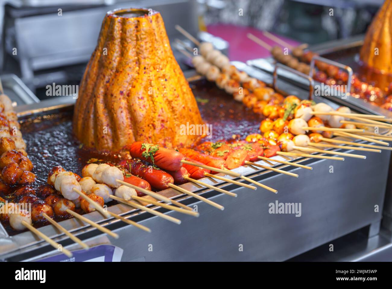 Boule de porc en brochettes comprenant des saucisses cuites sur un grill chaud, arrosées d'une sauce épicée, dans un marché alimentaire de rue. Banque D'Images