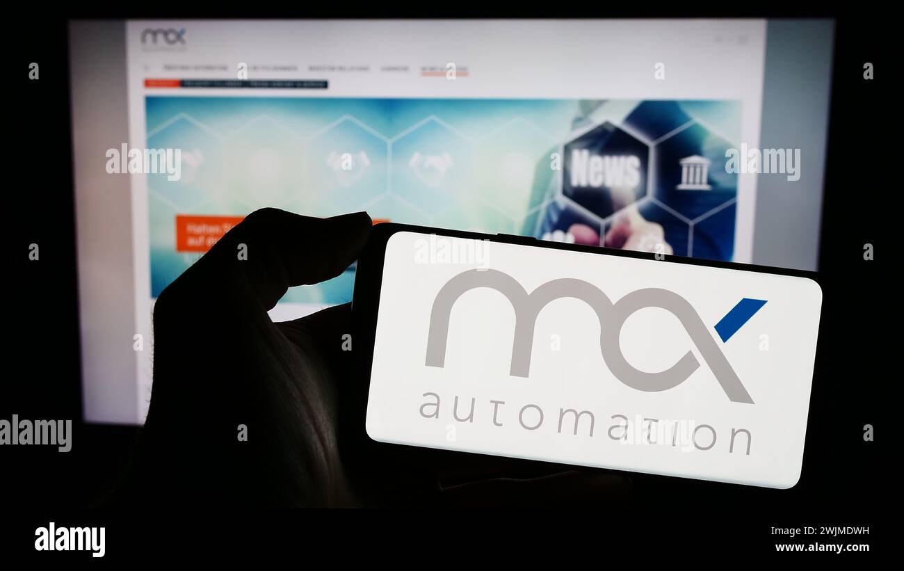 Personne tenant le téléphone portable avec le logo de la société d'ingénierie allemande MAX Automation se en face de la page Web de l'entreprise. Concentrez-vous sur l'affichage du téléphone. Banque D'Images