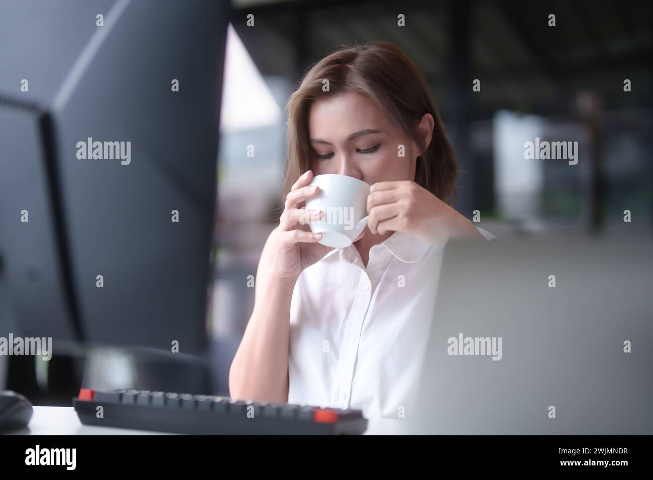 Femmes d'affaires asiatiques prennent une pause à boire du café et de la détente après avoir travaillé à taper des données sur ordinateur au sujet de la planification du rapport de marketing tout en un Banque D'Images