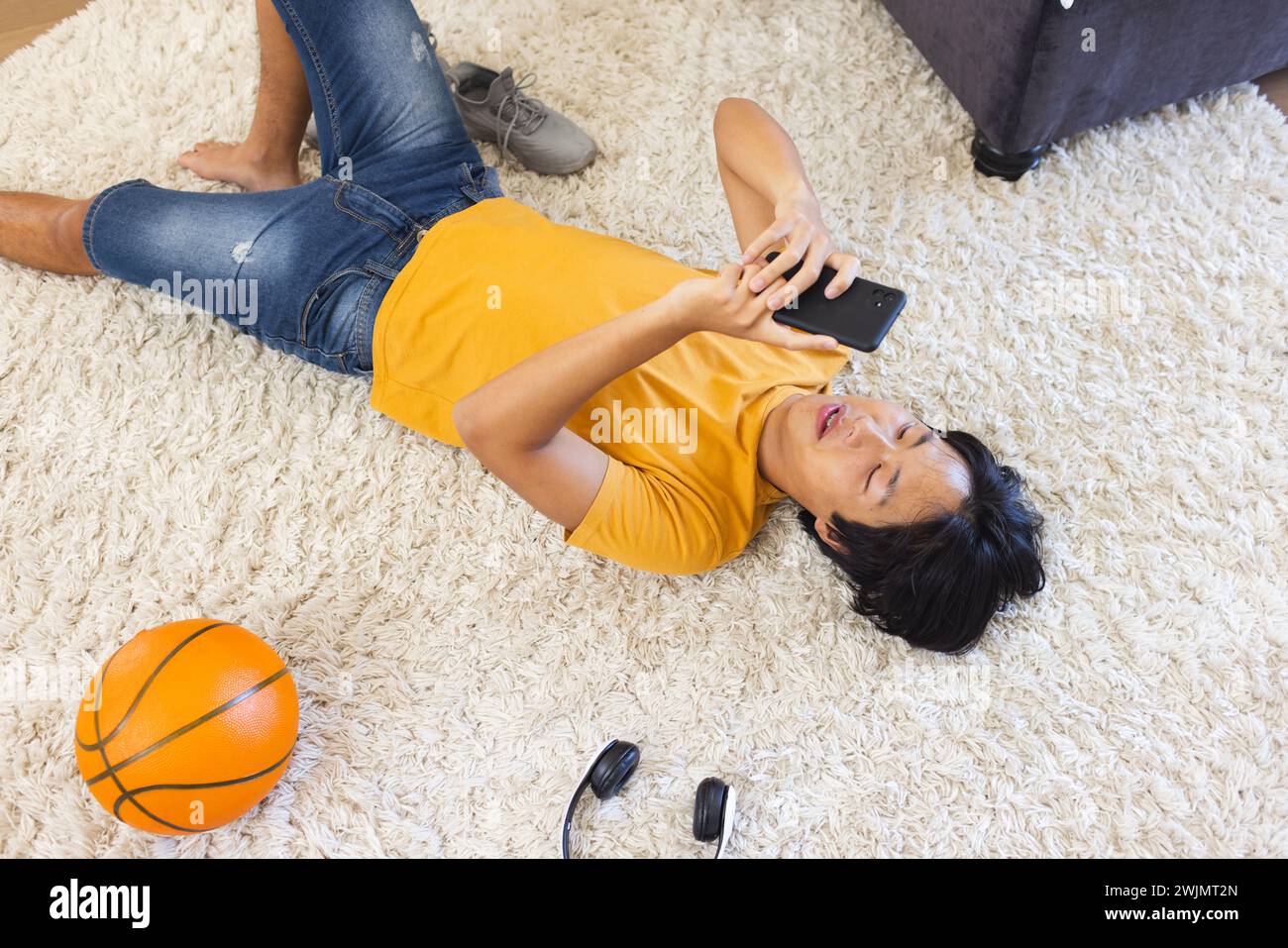 Adolescent asiatique allongé sur un tapis à la maison, en utilisant son smartphone Banque D'Images
