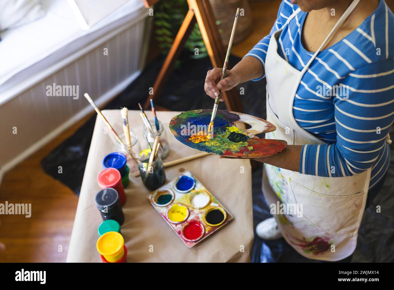 Une femme biraciale mature artiste mélange les couleurs de peinture à la maison, avec espace de copie Banque D'Images