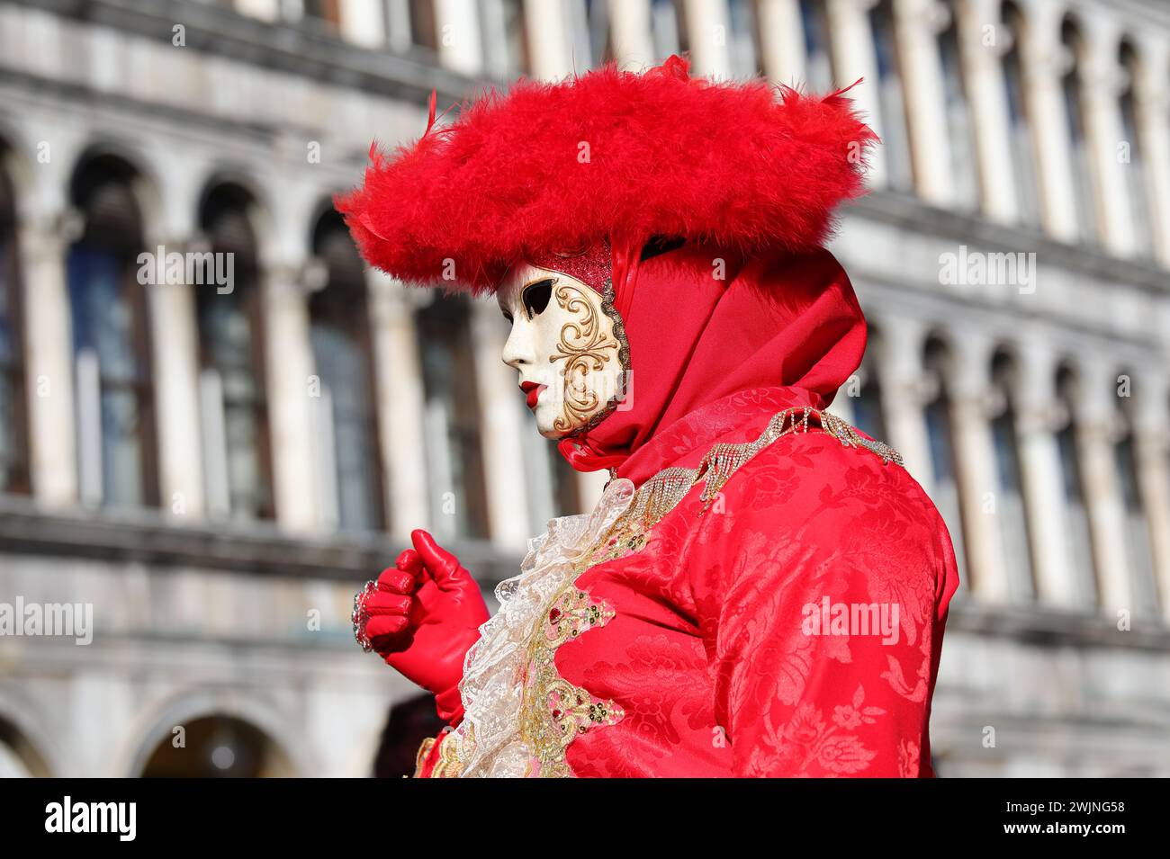 Venise, VE, Italie - 13 février 2024 : mascarade personne avec chapeau rouge et ancien palais sur le fond pendant le carnaval Banque D'Images