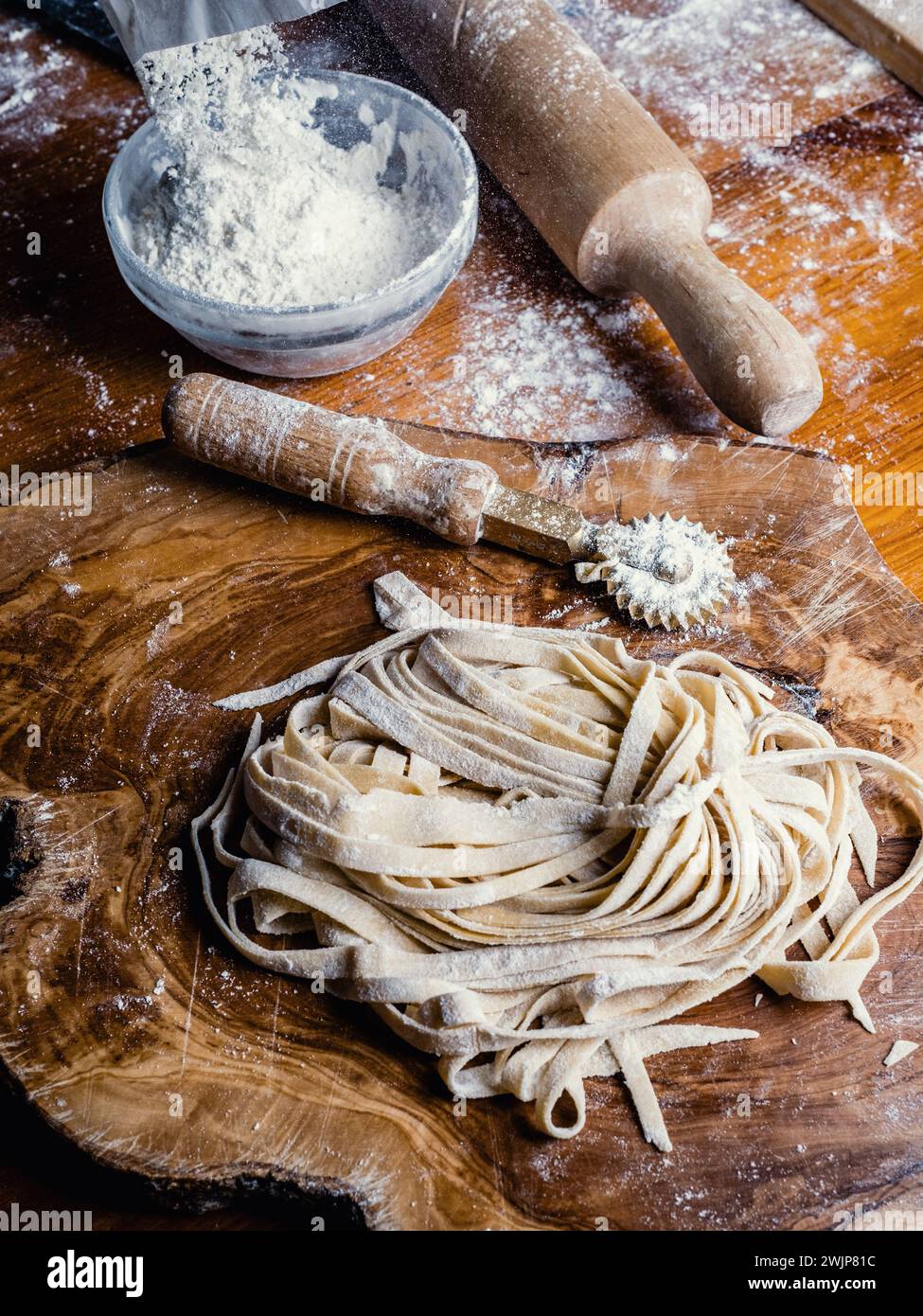 Gros plan de pâtes faites à la main appelées fettuccine, laissées reposer sur une planche à découper en bois. Quelques outils utiles : un rouleau à pâtisserie et un coupe-disque à pâtisserie. Banque D'Images