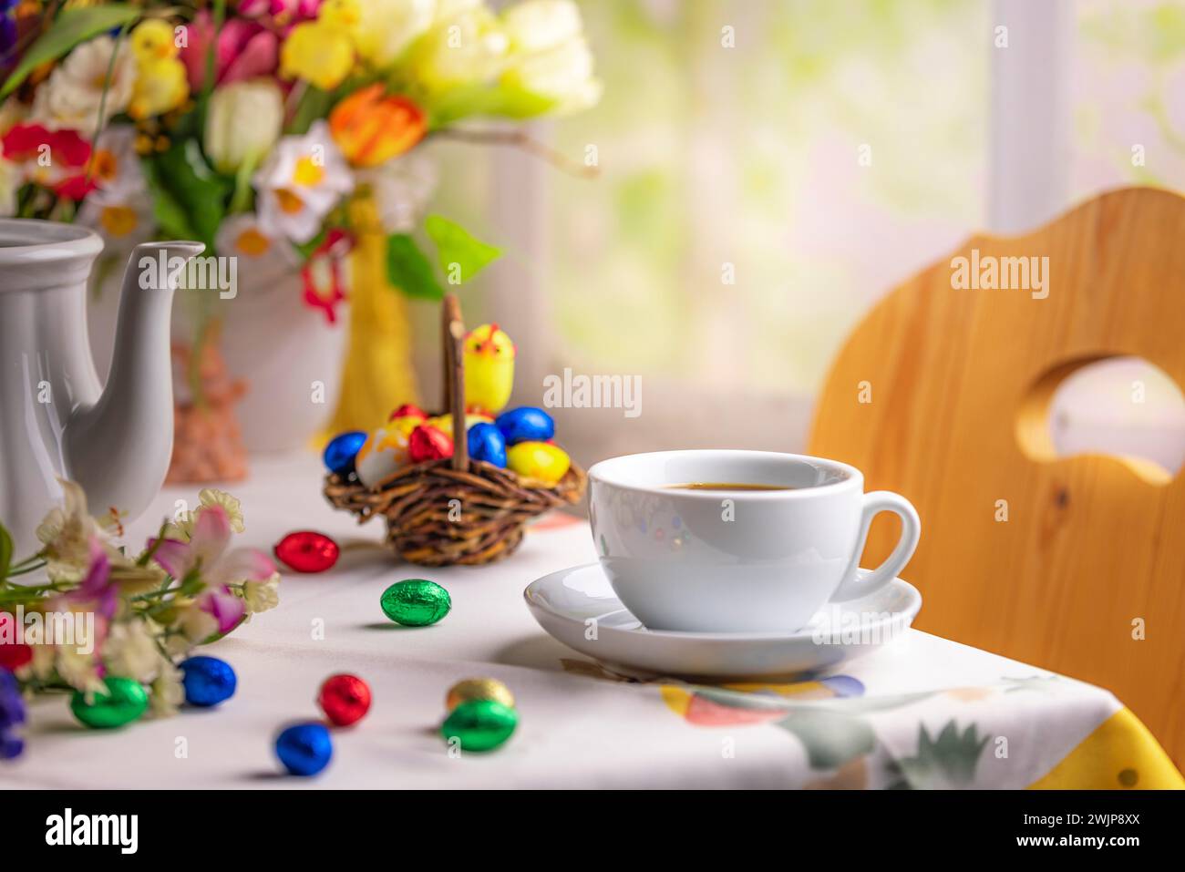 Une tasse à café sur une table avec des décorations de Pâques et un bouquet coloré de fleurs de printemps en arrière-plan Banque D'Images