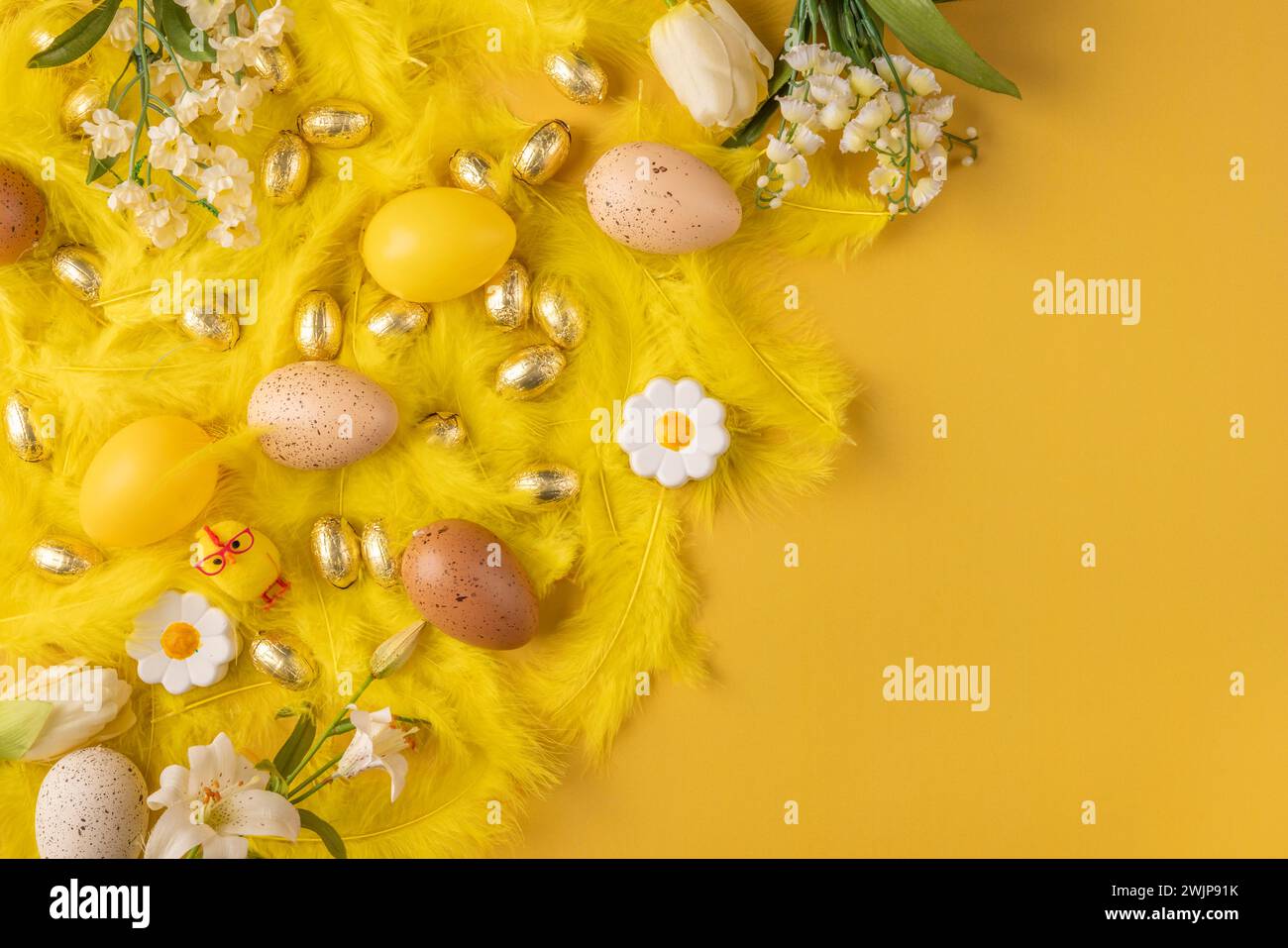 Décorations festives de Pâques avec des plumes jaunes, des œufs de Pâques jaunes et des fleurs de printemps sur fond jaune Banque D'Images