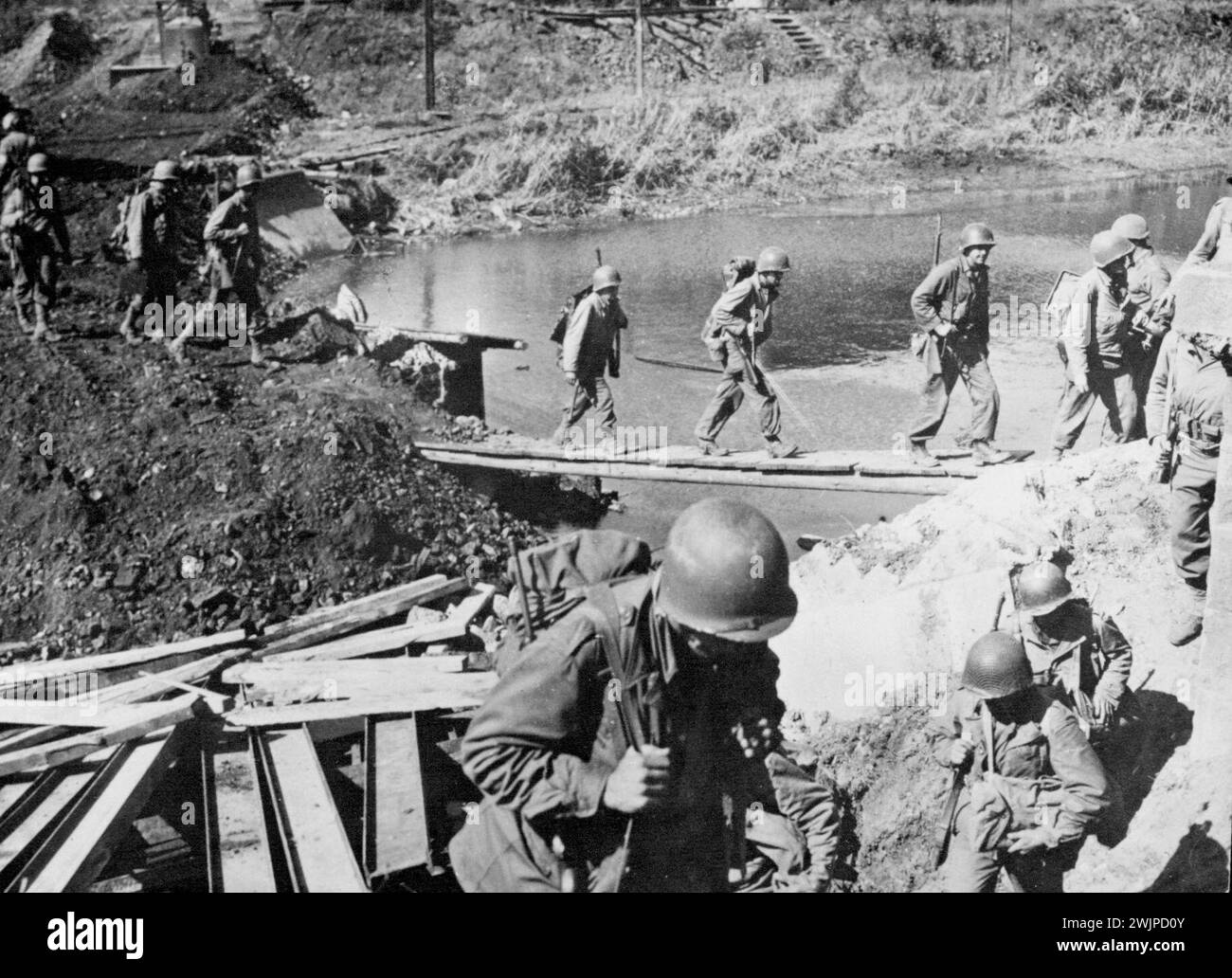 Les soldats américains traversent un canal français -- fichier d'infanterie américain à travers une passerelle improvisée sur un canal en France pour pousser vers la Moselle et la frontière allemande. Le 21 septembre 1944, les troupes américaines avaient pénétré la frontière allemande en au moins sept endroits, tandis que les forces aéroportées et terrestres alliées en Hollande menaçaient de flanquer l'extrémité nord de la ligne de défense ennemie. 9 octobre 1944. Banque D'Images