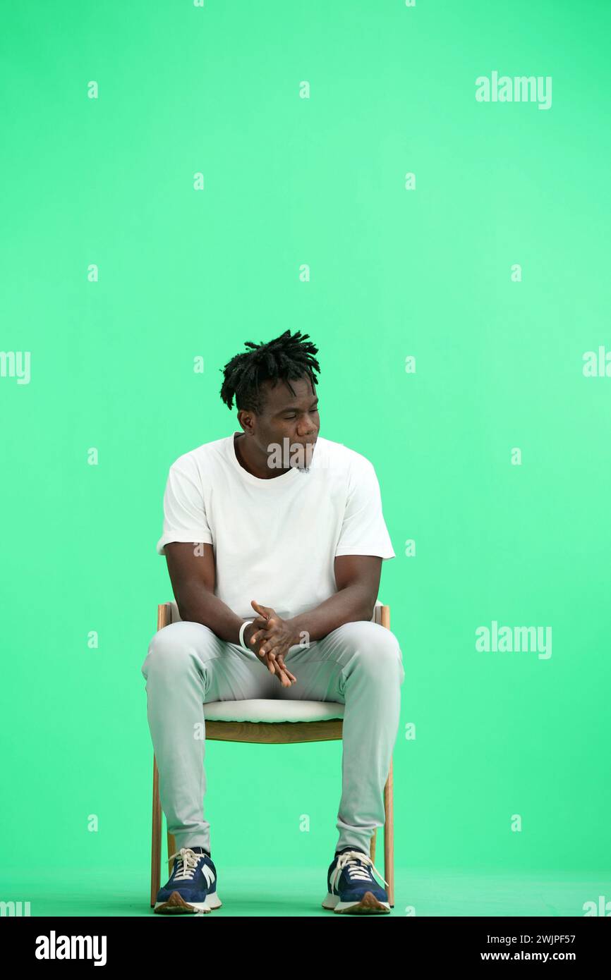Un homme, sur un fond vert, assis sur une chaise. Banque D'Images