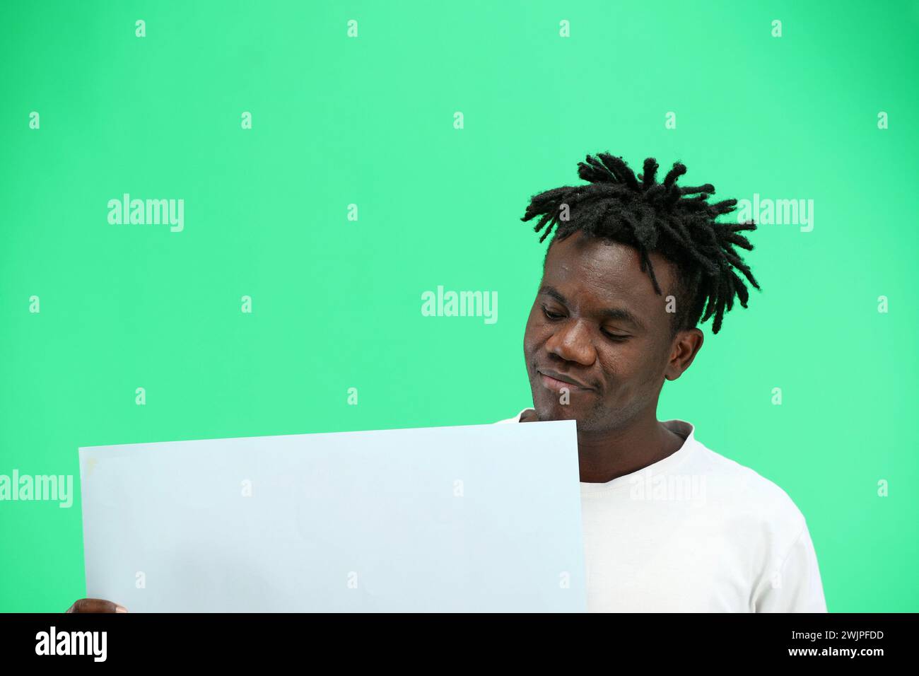Un homme, en gros plan, sur fond vert, montre une feuille blanche. Banque D'Images