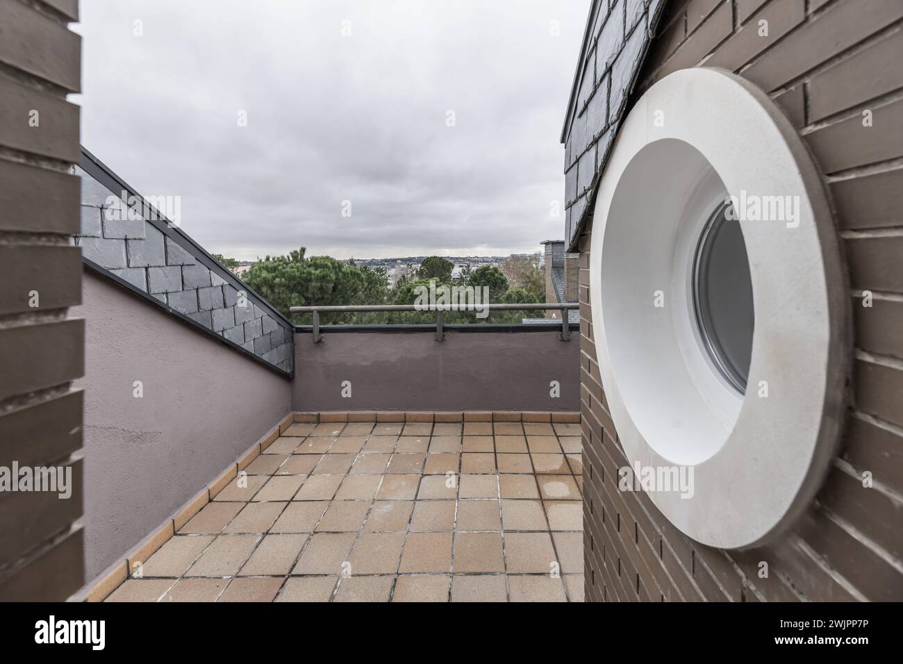 Terrasse d'une maison avec un hublot encadré blanc et les toits en pente d'une maison avec des tuiles d'ardoise noire et vue sur un parc avec beaucoup d'herbe et d'arbres Banque D'Images