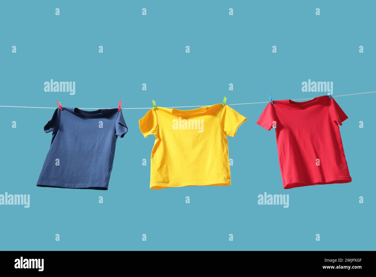 T-shirts colorés séchant sur la ligne de lavage sur fond bleu clair, vue d'angle bas Banque D'Images T-shirts colorés séchant sur la ligne de lavage sur fond bleu clair, vue d'angle bas Banque D'Images