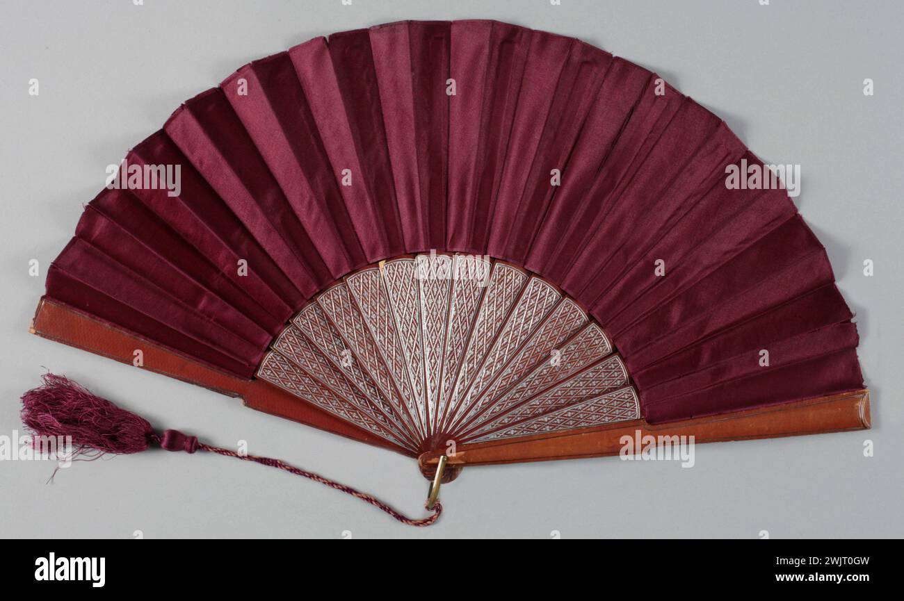 Ventilateur plié, monture estampillée avec un motif écrasé de fleurs stylisées argentées. GAL2001.272.1 feuille de satin Bordeaux, bélière en métal doré, gland de soie Bordeaux, cadre en cuir rouge estampé Banque D'Images
